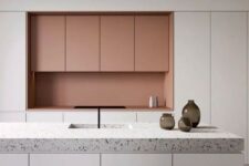 a minimalist white and coral kitchen with no handles and a grey terrazzo countertop that adds pattern to the space