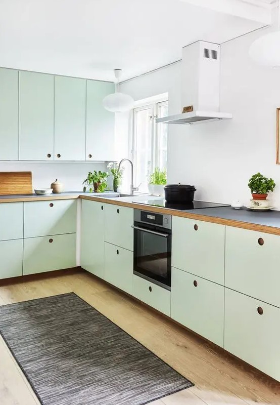 a mint green kitchen with plywood cabinets, a white backsplash, black countertops, no handles and built-in appliances