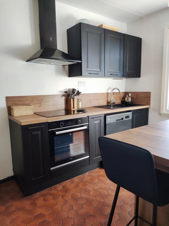 a modern black kitchen with a terracotta tile floor, black cabinets, butcherblock countertops and a backsplash is a bold and catchy space