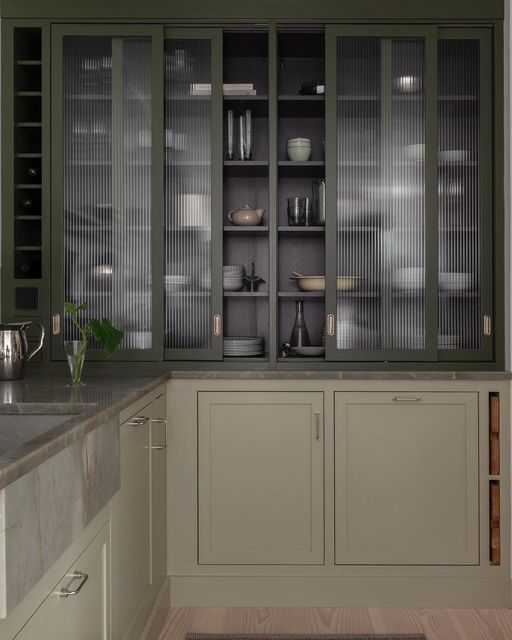 a modern classic greige kitchen with grey stone countertops and dark green fluted glass cabinets with sliding doors