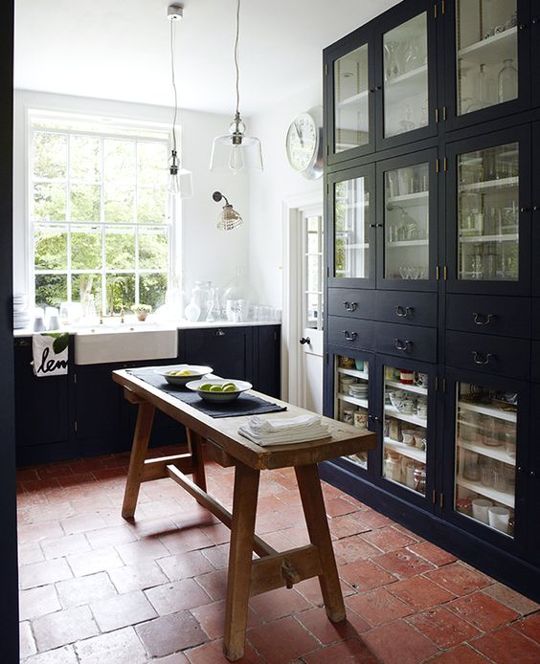 a modern farmhouse bathroom clad with terracotta tiles, with black cabinets and a rough wood table that is a kitchen island