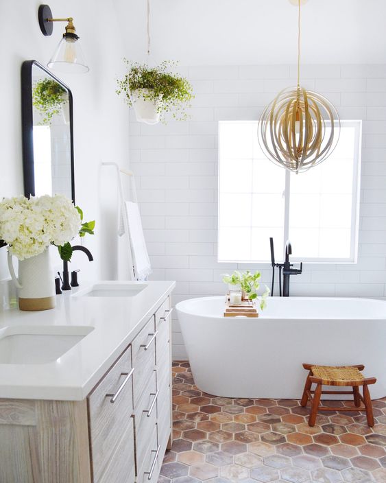 a modern farmhouse bathroom with white tile walls and a terracotta hex tile floor, a whitewashed vanity, an oval tub and greenery