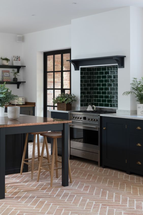 a modern farmhouse kitchen in black and white, with a terracotta tile floor, black cabinets and a large table as a kitchen island