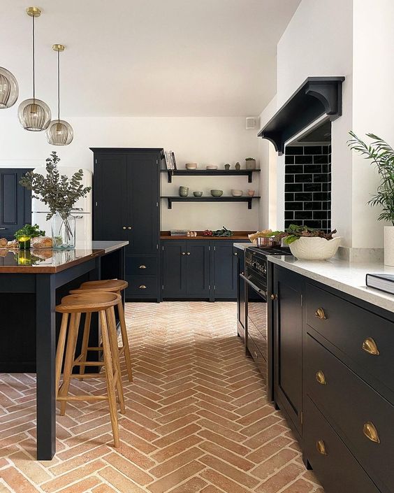 a modern farmhouse kitchen with a terracotta tile floor, black cabinets, a large kitchen island, pendant lamps
