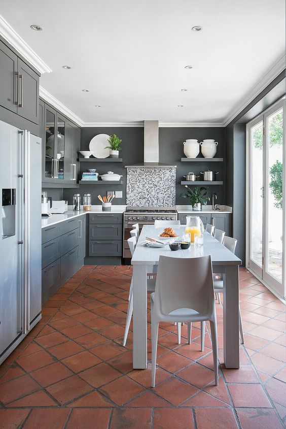 a modern grey kitchen with a glazed wall, a terracotta tile floor, graphite grey cabinets and a white dining set