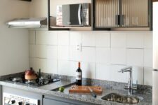a modern kitchen with flat panel and fluted glass cabinets, grey granite countertops, black framing and white square tiles