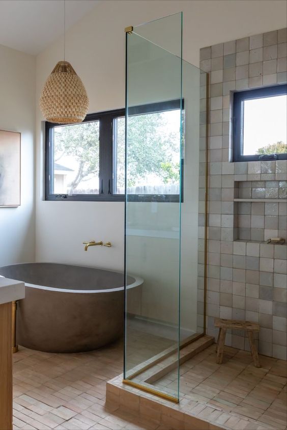 a modern rustic bathroom clad with terracotta tiles and neutral Zellige ones, an oval stone tub, a woven pendant lamp