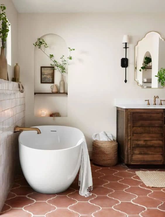 a modern rustic bathroom with white plaster walls and a terracotta tile floor, a stained vanity, an oval tub and greenery