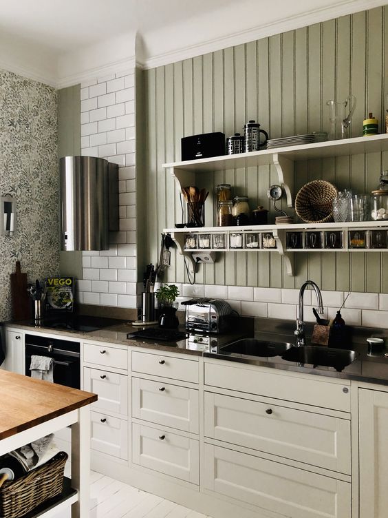 a modern rustic kitchen with neutral shaker cabinets, a grey soapstone countertop, a white tile backsplash and a green beadboard wall