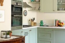a modern sage green kitchen with shaker cabinets and glass front ones, a white backsplash and countertops plus a vintage sideboard