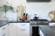a modern white farmhouse kitchen with shaker cabinets, black soapstone countertops and a black hood over the cooker
