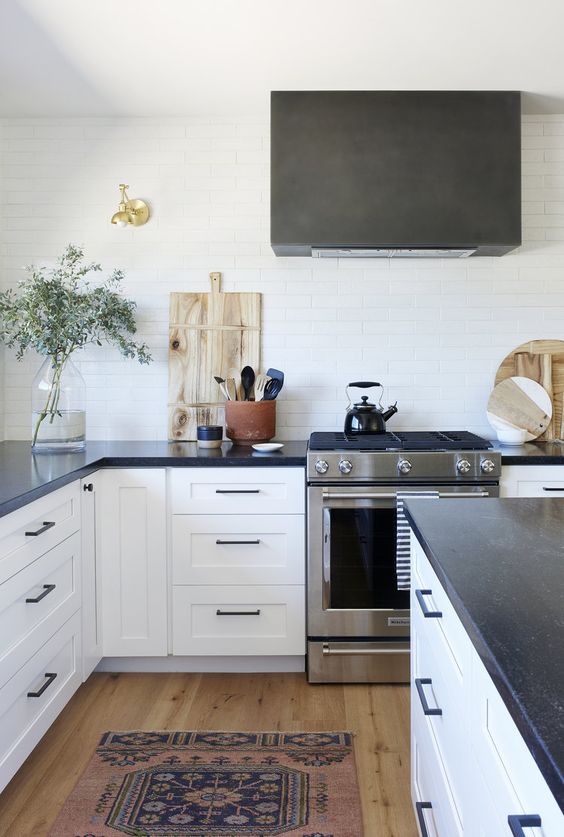a modern white farmhouse kitchen with shaker cabinets, black soapstone countertops and a black hood over the cooker