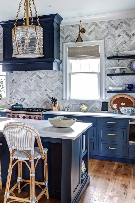 a navy kitchen with shaker cabinets, a neutral marble tile chevron backsplash, neutral granite countertops and tall stools