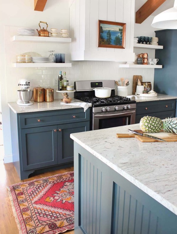 a navy kitchen with shaker cabinets, open shelving, a hood clad with wooden slats, white granite countertops and stained beams