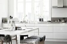 a neutral Nordic kitchen with sleke white cabinets, metal countertops, a white table and wooden benches plus pendant lamps