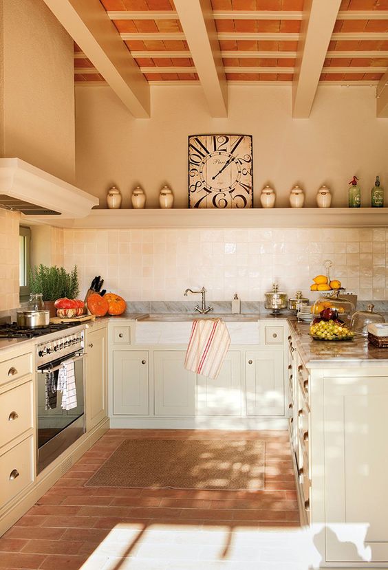 a neutral Provence kitchen with a terracotta tile floor, tan cabinets, a large hood and a white Zellige tile backsplash
