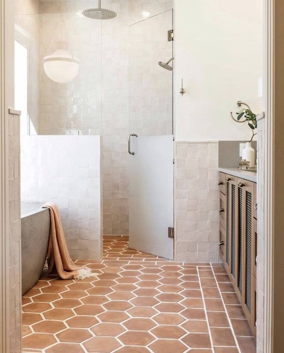 a neutral bathroom clad with white Zellige tiles, with a shower space and an oval tub, a terracotta tile floor, a stained vanity