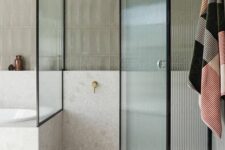 a neutral bathroom with a shower space enclosed in glass, with fluted glass doors and black framing is a chic and lovely idea