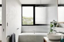 a neutral contemporary bathroom with grey granite tiles, a bathtub and a shower space with a fluted glass space divider, a large window