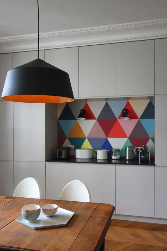a neutral contemporary kitchen with sleek cabinets, a colorful geo tile backsplash, a black pendant lamp and a wooden table