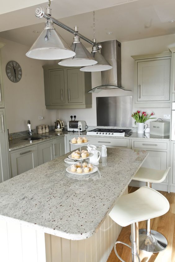 a neutral kitchen with light green cabinets with shaker cabinets, a white slat kitchen island, grey granite countertops and cool pendant lamps