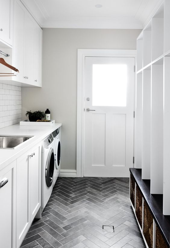 a neutral mudroom laundry with an open storage unit, baskets, white shaker cabinets, white countertops and a white subway tile backsplash
