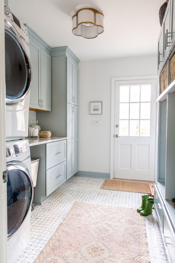 a pale blue mudroom entry with shaker cabinets, an open storage unit with baskets, printed rugs, a washing machine and a dryer