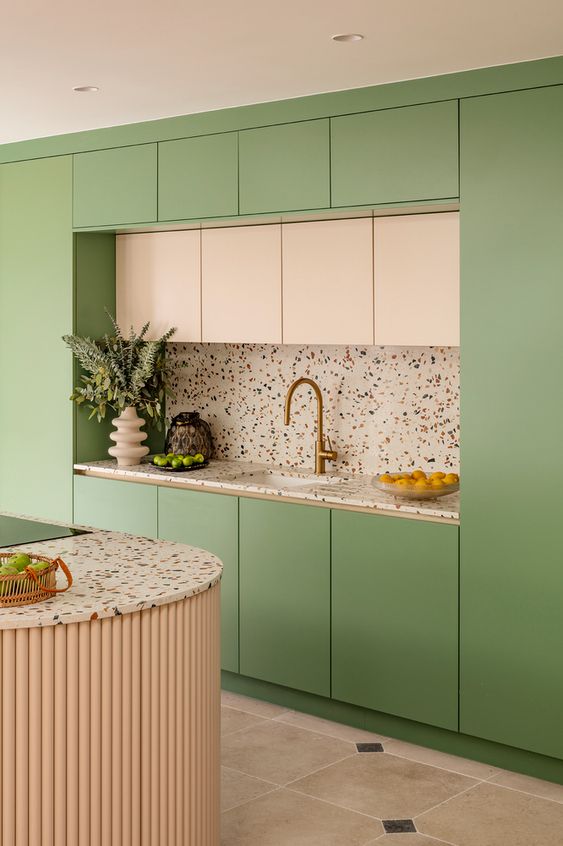 a pastel kitchen with creamy and light green flat panel cabinets, white terrazzo countertops and a fluted kitchen island