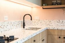 a pastel kitchen with white and stained fluted cabinets, white terrazzo countertops and a backsplash, black fixtures