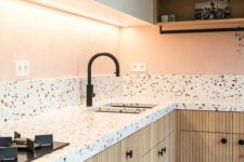 a pastel kitchen with white and stained fluted cabinets, white terrazzo countertops and a backsplash, black fixtures