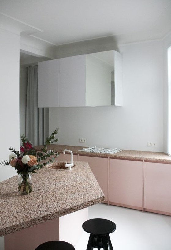 a pink and white kitchen with pretty pink terrazzo countertops and a geometric kitchen island plus black stools