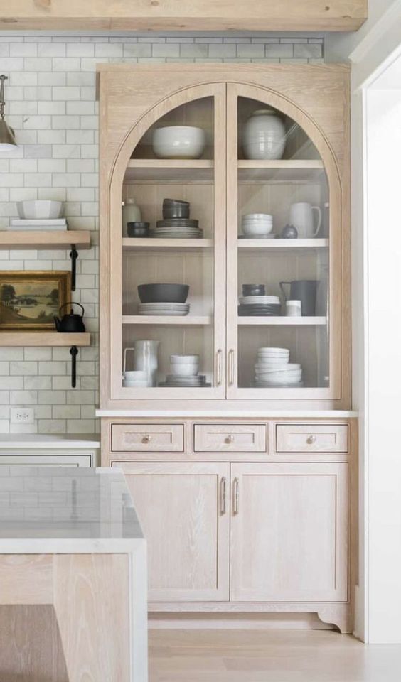 a pretty grey and stained kitchen with shaker, inlay and glass arched cabinets, a white subway tile backsplash and white countertops