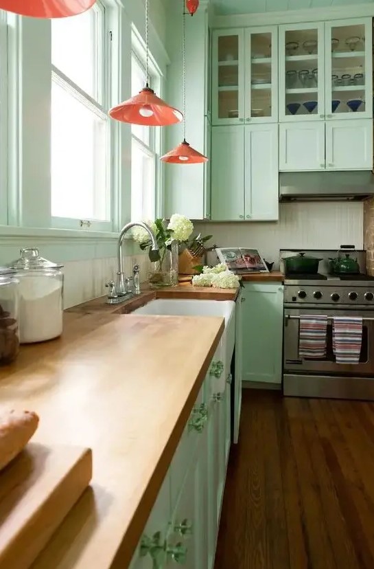 a pretty mint green kitchen with a white beadboard backsplash, butcherblock countertops, red pendant lamps and green knobs