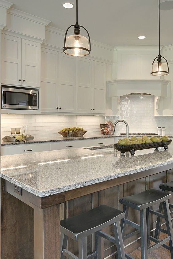 a pretty white kitchen with shaker cabinets, a white subway tile backsplash, a stained kitchen island and grey granite countertops