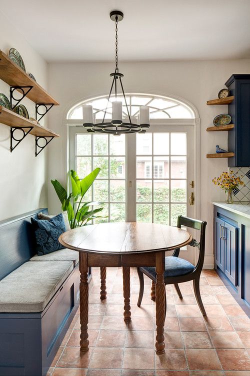 a refined vintage breakfast nook with a terracotta tile floor, a blue banquette seating and a chair, a stained table and a chic chandelier