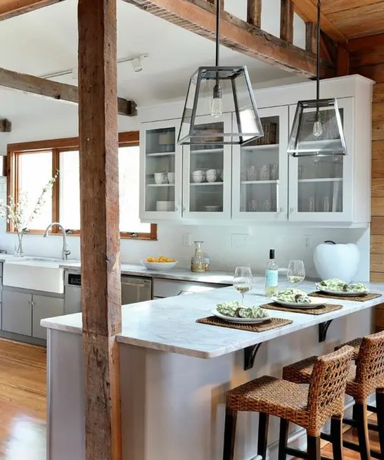 a relaxed beach kitchen with dove grey sleek cabinets, white stone coutnertops, wooden beams and lovely woven stools