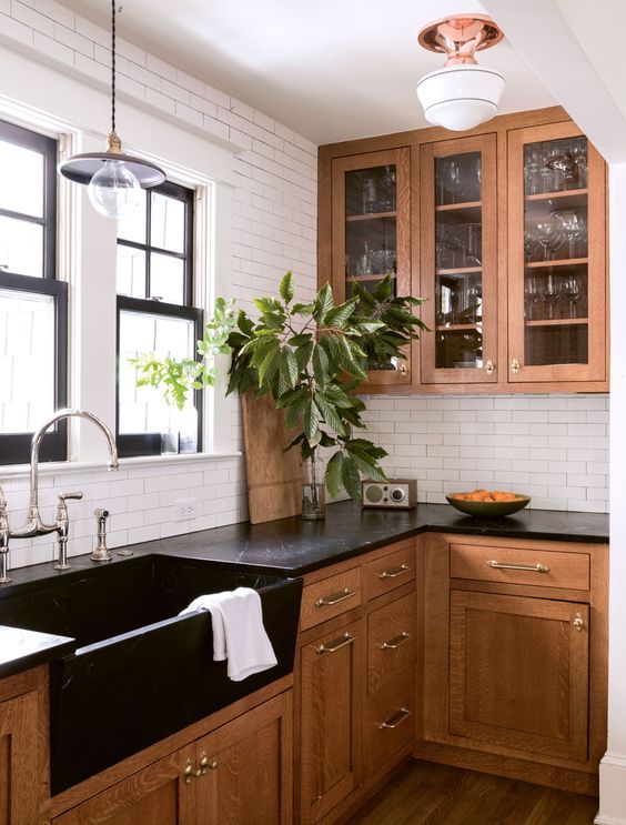 a rich-stained kitchen with shaker and glass cabinets, black quartz countertops, a white subway tile backsplash is elegant and chic