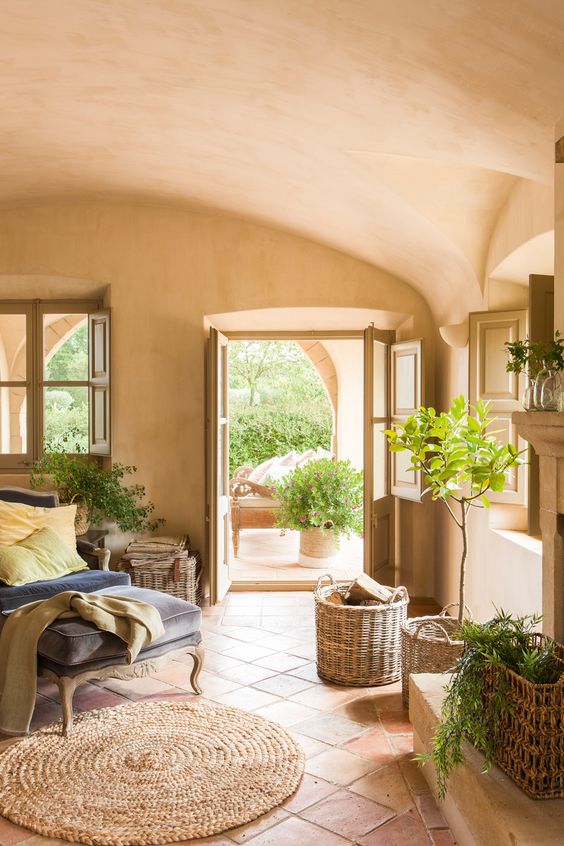 a rustic Spanish style liivng room with terracotta tiles and plaster walls and a ceiling, a refined daybed, baskets and potted plants