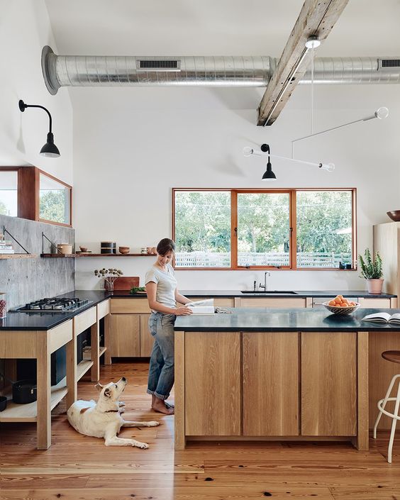 a rustic kitchen with stained cabinets and a kitchen island, black soapstone countertops and lots of natural light in it