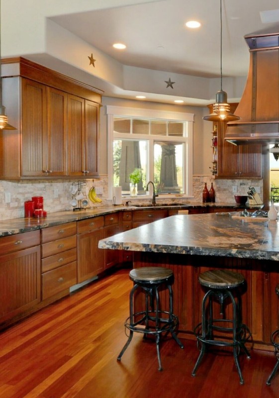 a rustic rich-stained kitchen with shaker and fluted cabinets, a neutral tile backsplash and bold black and gold granite countertops with huge veins