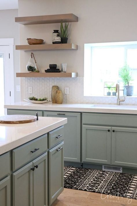 a sage green farmhouse kitchen with shaker cabinets, open shelves instead of upper cabinets, a large kitchen island and black fixtures