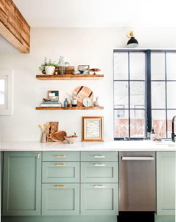 a sage green farmhouse kitchen with shaker cabinets, open shelves, white stone countertops, wooden beams and black framed windows