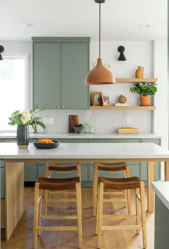 a sage green kitchen with open shelves and only lower cabinets, a kitchen island that doubles as a dining table