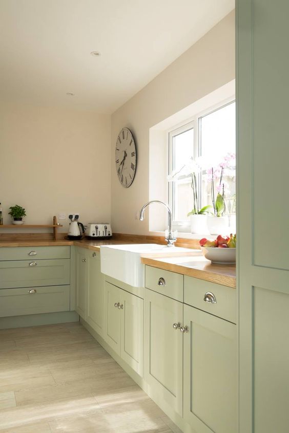 a sage green kitchen with shaker cabinets, butcherblock countertops, no upper cabinets for an airy feeling in the space