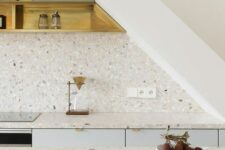 a serene white and pale blue kitchen with white terrazzo countertops and a backsplash, white pendant lamps