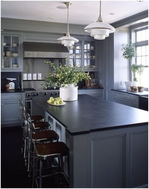 a slate grey kitchen with shaker cabinets, black soapstone countertops, metal stools and pendant lamps