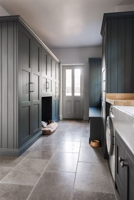 a slate grey mudroom laundry with shaker cabinets, a storage bench, a pet bed and a washing machine and a dryer