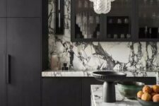 a sophisticated black and white kitchen with matte black cabinets and white marble countertops and a backsplash plus a stunnign crystal chandelier