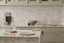 a sophisticated greige kitchen with flat panel and glass cabinets, white terrazzo countertops and a backsplash