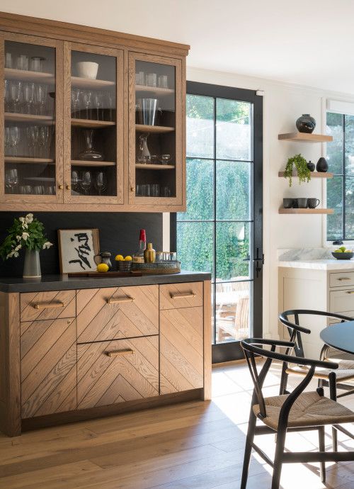 a stained kitchen with chevron and glass front cabinets, black countertops and a backsplash and an eating zone right here